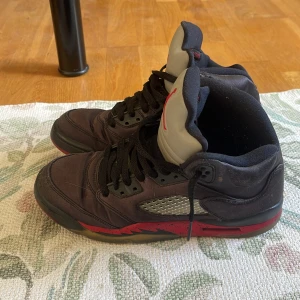 Svarta Nike Air Jordans med röda detaljer - Säljer ett par svarta Nike Air Jordans med röda detaljer och svart snörning. Skorna har en hög modell, meshpanel på sidan och en platt sula. Perfekta för dig som gillar streetwear och sneakers med attityd.