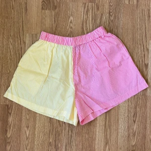 Randiga shorts från Gina Tricot - Färgglada shorts från Gina Tricot med elastisk midja. Ena sidan är gul och den andra rosa, båda med vita smala ränder.