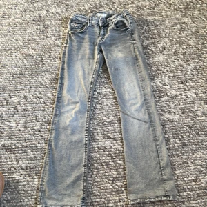 Grå jeansbyxor från Gina Tricot - Säljer ett par grå jeansbyxor från Gina Tricot i klassisk femficksmodell. Byxorna har utsvängda ben, snygga bakfickor med lock och knapp samt normal passform. Perfekta till vardags och lätta att matcha med olika toppar.