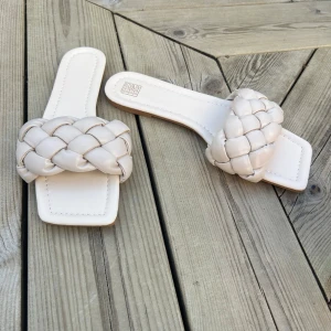 Vita flätade sandaler med fyrkantig tå - Säljer ett par trendiga vita sandaler med bred, flätad rem och fyrkantig tå. Skorna har platt sula och öppen design, perfekta för varma dagar. Snygga att matcha till sommarens outfits!