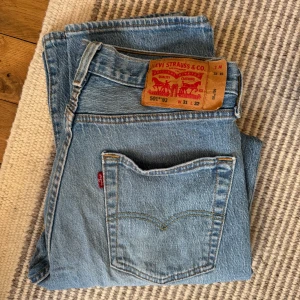 Levi's 501 93 ljusblå jeans - Klassiska ljusblå Levi's 501 jeans med raka ben och femficksdesign. Ikonisk läderpatch bak och röd Levi's-tagg på bakfickan. Perfekta för en avslappnad stil och tidlös denimlook. 