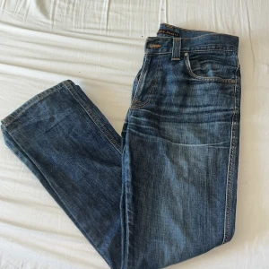 Blå jeans från Nudie Jeans - Klassiska blå jeans från Nudie Jeans med raka ben och snygga kontrastsömmar. Byxorna har fyra fickor och detaljerade bakfickor med Nudie Jeans signatursöm. Perfekta för en avslappnad stil. 