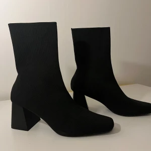 Svarta stretchiga boots med klack - Säljer ett par svarta boots med stretchigt tyg och bred klack. Skorna har en minimalistisk design med rund tå och är perfekta för dig som gillar stilrena och moderna skor.