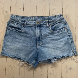 Blå jeansshorts med fransar från LAB (Kappahl) - Snygga blå jeansshorts från LAB Industries med råa fransade kanter och klassisk femficksdesign. Shortsen har normal passform och knappgylf. Perfekta för sommardagar och enkel att matcha med olika toppar. dessa är 170 dem är även runt storleken 36.