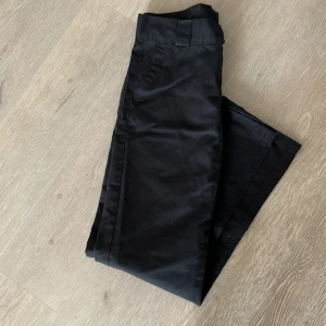 Svarta kostymbyxor från Sweet Skins - Svarta kostymbyxor från Sweet Skins med klassisk rak passform och diskreta bakfickor. Byxorna har hällor för bälte och är tillverkade i ett slätt material som känns dressat och stilrent.