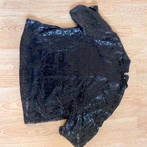 Svart glittrig topp med paljetter - Säljer en svart glittrig topp från H&M, täckt med paljetter som ger ett riktigt festligt intryck. Toppen har korta ärmar och en rund halsringning. Perfekt för dig som vill sticka ut på festen!