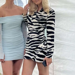 Zebramönstrad omlottklänning med krage - Säljer en snygg zebramönstrad klänning med omlottkänsla och krage. Klänningen har långa ärmar och svartvita ränder som ger ett coolt intryck. Perfekt för dig som vill sticka ut med en trendig look.