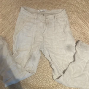 Beige linnebyxor från Zara  - Säljer ett par ljusbeige linnebyxor med klassisk design och normal passform. Byxorna har knapp och dragkedja framtill samt bälteshällor. Perfekta för varmare dagar och ger en avslappnad men stilren look.