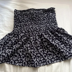 Mörkblå blommig kortkjol från Gina Tricot - Supersöt mörkblå  kortkjol från Gina Tricot med vitt blommigt mönster och smock i midjan. Kjolen har en luftig och lätt form som passar perfekt till varma dagar. Enkel att matcha med olika toppar för en trendig look. Nypris 279, knappt använd 🦋