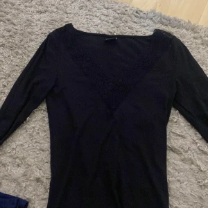 Svart långärmad topp med spets från Gina Tricot - Svart långärmad topp från Gina Tricot med v-ringning och fina spetsdetaljer längs ringningen. 