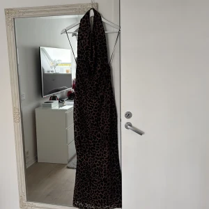 Leopardmönstrad långklänning med öppen rygg - Säljer en snygg långklänning med leopardmönster och djup v-ringning. Klänningen har öppen rygg och smala axelband som knyts i nacken. Perfekt för dig som vill sticka ut med ett djuriskt mönster. Materialet känns mjukt och följsamt. Den är oanvänd och säljs just därför, den är från ginatricot.  Peferkt för eleganta kvällar