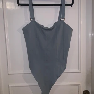 Ljusblå body från H&M - En stilren ljusblå body från H&M med justerbara axelband och enkel design. Baddräkten har en mjuk, något draperad urringning och är tillverkad i ett stretchigt material som ger en bekväm passform.