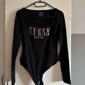 Svart långärmad bodysuit från Guess - Svart långärmad bodysuit från Guess med silvrig logotyp och texten 'Since 1981' framtill. Storlek M men känns som S. Enbart testat en gång💕