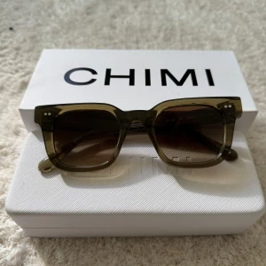 Chimi 04 gröna - Snygga solglasögon från CHIMI med fyrkantig form och transparent grön båge. Glasen är mörktonade och bågarna har små silvriga detaljer vid hörnen. Perfekt accessoar för att lyfta din stil. Nästan helt nya, använda bara ungefär 4 gånger 👌