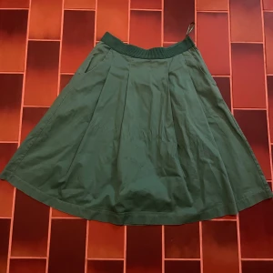 Grön kjol från Lindex, storlek 38 - Grön kjol från Lindex i storlek 38. Kjolen har en bred, ribbad midjeresår och är lätt utställd med fina veck. Perfekt för dig som gillar en enkel men snygg stil. Materialet känns mjukt och skönt mot huden.