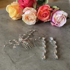 Silverfärgat hårsmycke & örhängen - Säljer ett set med ett glittrigt silverfärgat hårsmycke med små blommor och kristaller samt matchande långa örhängen med droppformade stenar. Perfekt för att ge en extra touch till din look.
