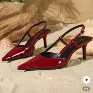 Vinröda lackade pumps med klack - Snygga vinröda pumps i lackad syntet med spetsig tå och smal klack. Skorna har öppen häl med justerbar rem och ger en riktigt trendig vibe. Perfekta för dig som vill sticka ut med en elegant och edgy look.