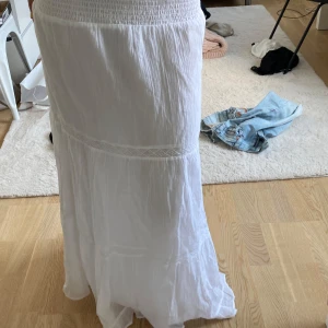 Vit långkjol med smock och spetsdetaljer - Superfin vit långkjol från gina tricot med smock i midjan och tunna spetsdetaljer. Kjolen är luftig och har en flowy känsla, perfekt för varma dagar. Tillverkad i mjuk bomull som känns skön mot huden.