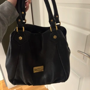 Svart Marc by Marc Jacobs handväska!  - Ge gärna prisförslag! Pris går att diskutera!    Säljer en svart handväska i skinn från Marc Jacobs med snygga guldfärgade metalldetaljer och dubbla handtag. Väskan har ett coolt innerfoder med logotyptryck och dragkedjefack. Perfekt storlek för allt du behöver ha med dig. Väskan är i bra skick! Ingen dustbag ingår. 