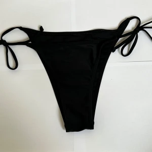 Bikini underdel - Snygga svarta bikiniunderdelar med högt skuren modell och knyt i sidorna. Klassisk och stilren design som passar perfekt till stranden eller poolen. Materialet är mjukt och stretchigt för en bekväm passform 