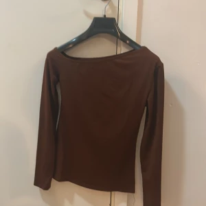 Brun långärmad topp med bred ringning - Säljer en stilren brun långärmad topp med bred, något båtformad ringning. Toppen har en slät och stretchig känsla, perfekt att styla med jeans eller kjol. Enkel design utan mönster eller detaljer, vilket gör den lätt att matcha.