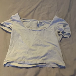 Ljusblå croppad topp från Boohoo - En ljusblå croppad topp från Boohoo med bred, rundad urringning och korta ärmar. Enkel och stilren design i mjuk bomull, perfekt för att matcha med jeans eller kjol. Snygg passform som ger en avslappnad vibe.