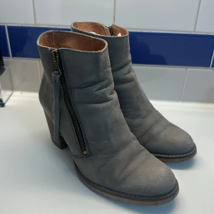 Gråa boots i skinn med dragkedja - Snygga grå boots i skinn med rund tå och robust klack. Dragkedja på sidan med råa detaljer och träfärgad klack ger en cool look. Perfekta till jeans eller klänning för en trendig stil.