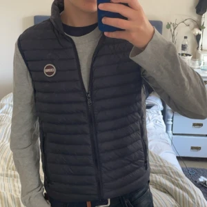 Mörkblå dunväst från Colmar - Säljer en mörkblå dunväst från Colmar med quiltad design och dragkedja framtill. Västen har en hög krage och en rund Colmar-logga på bröstet. Perfekt att slänga över en hoodie eller t-shirt för en chill look. Pris kan diskuteras 
