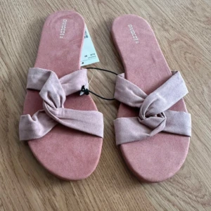 Rosa sandaler med knut från H&M - Snygga sandaler från H&M i ljusrosa mockaliknande material. De har breda band med en cool knutdetalj över foten och platt sula. Perfekta för varma dagar när du vill ha en chill och trendig look
