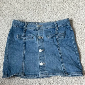 Blå jeanskjol med knappar från Lindex - Snygg blå jeanskjol från Lindex med knappar framtill och bälteshällor. Strl 134/140 men är jätte stretchig och passar mig med strl S. 