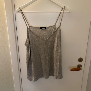 Grått linne från Bik Bok - Enkel och stilren grått linne från Bik Bok med smala axelband och v-ringning. Toppen är ärmlös och har en loose passform, perfekt för varma dagar. Mjuk och skön i bomullsmix som känns lätt mot huden.