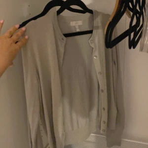 Beige kofta från H&M i bomull - En stilren beige kofta från H&M i storlek S. Koftan har rund halsringning, långa ärmar och knäppning framtill med små knappar. Tillverkad i tunn bomull, perfekt att slänga över en topp för en chill look.