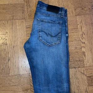 Blå skinny jeans från Jack & Jones - Säljer ett par blå skinny jeans från Jack & Jones i storlek 28/30. Jeansen har klassisk femficksdesign, snygga slitningar och en mörkare tvätt. Tillverkade i stretchig denim för en bekväm passform. Perfekta till sneakers och hoodie.