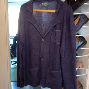 Marinblå cardigan jacka Alan Paine - Säljer en marinblå cardigan jacka från Alan Paine i 100% merinoull. Jackan har tre knappar framtill, två stora fickor nertill och en bröstficka. Den är stickad och har en klassisk krage, perfekt för dig som gillar stilren och bekväm look.