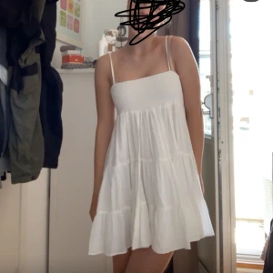 Vit Zara klänning  - Slutsåld Supersöt vit kortklänning med smockad överdel och tunna axelband. Klänningen har en luftig, volangig kjol och är perfekt för varma dagar. Enkel och stilren design som ger en fräsch look.