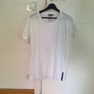 Vit basic t-shirt från Sail racing - En stilren vit t-shirt från Sail racing med rund halsringning och korta ärmar. Tillverkad i mjuk bomull och har en liten svart detalj nertill på framsidan. Perfekt för en clean och enkel look.