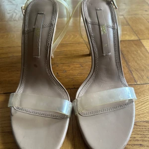 Beige klackade sandaler från Zara - Snygga beige sandaler från Zara med transparenta remmar och hög klack. Skorna har öppen tå och stilren design som ger en modern look.