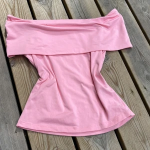Ljusrosa offshoulder tubtopp - Skriv innan köp!   Snygg ljusrosa tubtopp med bred offshoulder-krage. Toppen är axelbandslös och har en mjuk, stretchig passform som sitter skönt. Perfekt för dig som vill ha en enkel men trendig look.