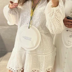 Vit broderad kortklänning med volang - Superfin vit kortklänning med broderade detaljer och volangkant. Klänningen har långa, vida ärmar och v-ringning. Perfekt för student eller sommarhäng! Söt och luftig modell med romantisk känsla. Nypris 599kr