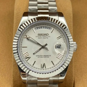Seiko Oyster Perpetual Day-Date klocka - Stilren Seiko Oyster Perpetual Day-Date med silverfärgad urtavla, romerska siffror och dag- och datumvisning. Klockan har ett robust armband i rostfritt stål och en räfflad bezel. Baksidan är transparent så du ser urverket. Perfekt för dig som gillar klassisk design.