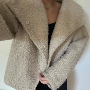 Beige teddyjacka med stora slag - Mysig beige teddyjacka med oversized passform och stora slag. Jackan har knäppning framtill med tryckknappar och är tillverkad i ett fluffigt teddy-material som ger en cool och avslappnad vibe. Perfekt för att hålla värmen under kyliga dagar.
