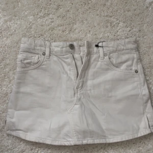 Vit jeanskjol från Zara - Säljer en snygg vit jeanskjol från Zara med klassisk femficksdesign, bälteshällor och knapp- samt dragkedjestängning framtill. Kjolen är kort och har raka linjer, perfekt till sommaren. Enkel och stilren look som passar till allt.