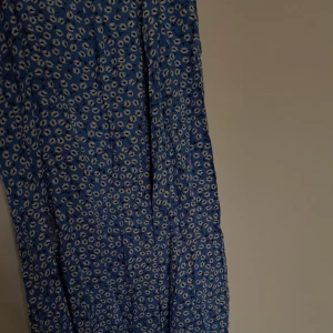 Blå blommig långkjol - Snygg blå långkjol med vitt blommigt mönster. Kjolen har en luftig känsla och är perfekt för varma dagar. Tyget är lätt och faller fint. Passar dig som gillar en feminin och trendig stil.