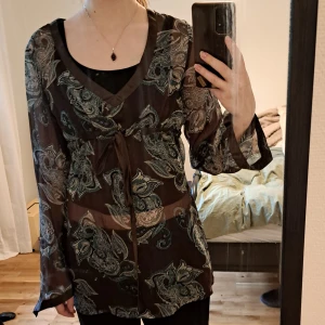 Brun mönstrad meshblus Esprit - En meshblus med paisleyinspirerat mönster i grönt och beige. Blusen har v-ringning, långa vida ärmar och ett knytband under bysten. Om ni vill se fler bilder eller har en fråga är det bara att höra av sig <3