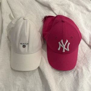GANT vit keps & New Era rosa NY keps - Två snygga kepsar: en klassisk vit GANT-keps i bomull med broderad logga framtill och justerbar rem bak, samt en rosa New Era 9FORTY keps med vit NY-brodyr, också i bomull och justerbar passform. Perfekta accessoarer för en sportig och trendig look. Mycket snygga 