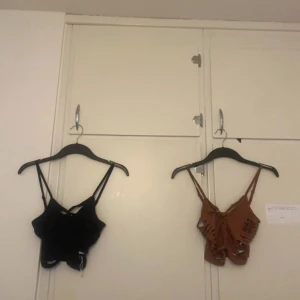 Brun och svart croppad linnetopp med flätor - Säljer en brun och svart croppad linnetopp med smala axelband, flätad detalj i ryggen och coola slitsar på sidorna. Toppen har en edgy look och är perfekt för dig som vill sticka ut. Materialet känns mjukt och lätt, perfekt för varma dagar. 