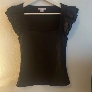Topp med volangärmar - Supersnygg svart topp i storlek XS. Toppen har fyrkantig ringning och coola volangärmar som ger en extra touch. Säljer då jag aldrig använder den🖤