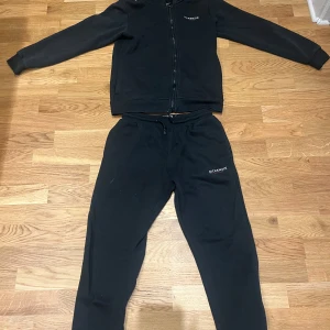 Svart tracksuite från McKenzie - Svarta tracksuite från McKenzie med dragsko i midjan och logga på vänster lår. Sköna och avslappnade med normal passform, perfekta för chill eller träning. Tillverkade i mjukt material som känns bekvämt hela dagen.