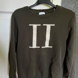 LES DEUX Sweatshirt - Olivgrön sweatshirt från Les Deux med stort vitt II-tryck framtill. Tröjan har rund halsringning, ribbade muddar och är långärmad. Perfekt för dig som gillar stilren och enkel design med en twist. Materialet känns mjukt och skönt mot huden.