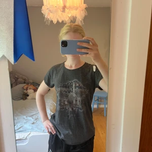 Mörkgrå t-shirt med tryck Gina Tricot - Säljer en mörkgrå t-shirt från Gina Tricot med coolt tryck framtill i rockstil. T-shirten har rund hals, korta ärmar och en normal passform. Perfekt för dig som gillar en avslappnad look